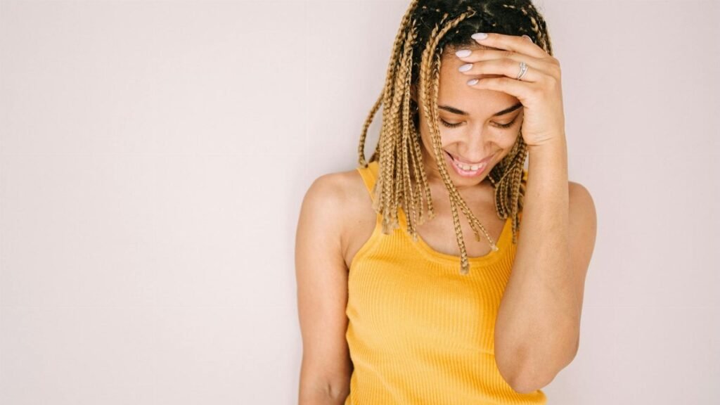 A joyful young woman in a stylish yellow top, smiling and touching her hair.