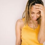 A joyful young woman in a stylish yellow top, smiling and touching her hair.