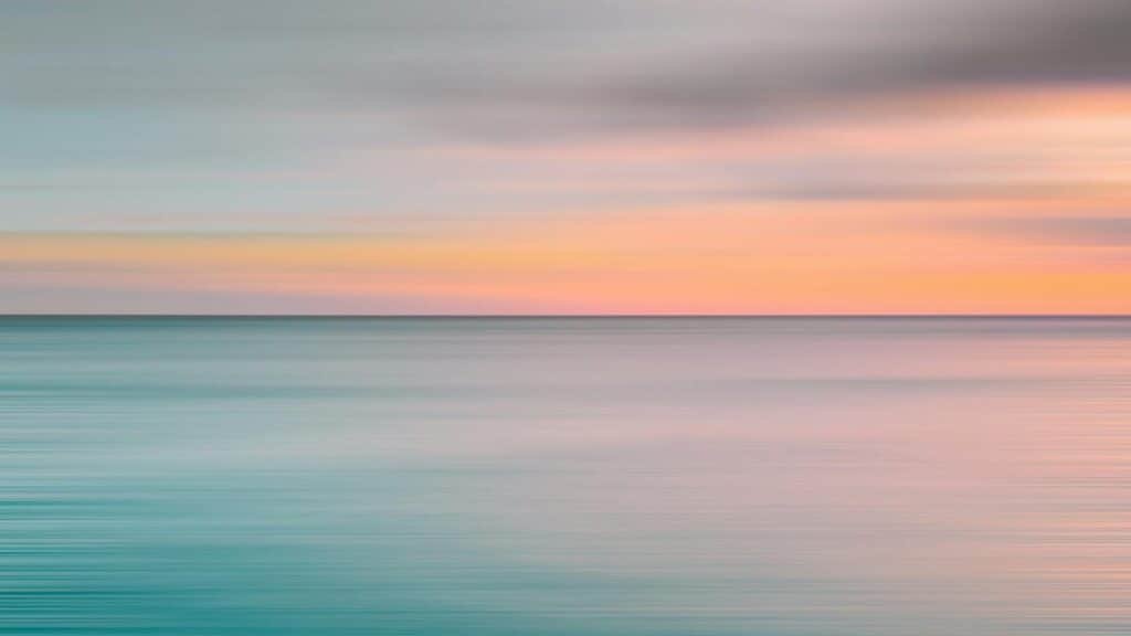 Tranquil ocean view during sunset with soft pastel colors over the horizon.