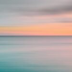 Tranquil ocean view during sunset with soft pastel colors over the horizon.