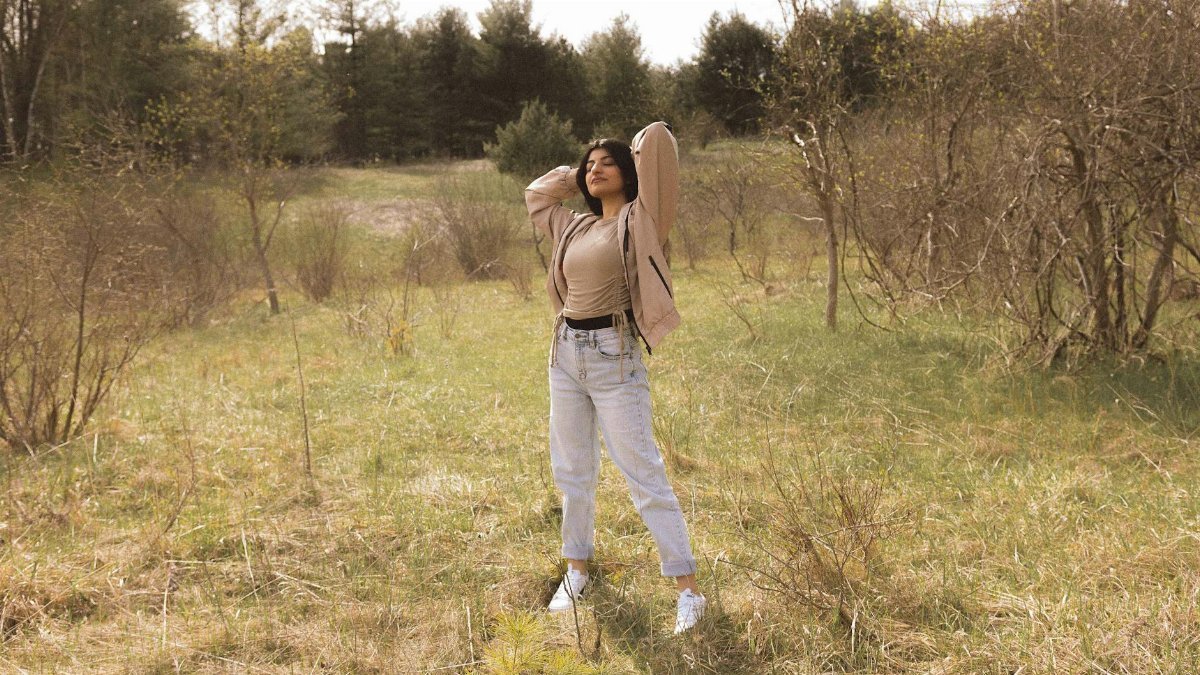 A woman standing with arms raised in a sunlit field, embracing nature.