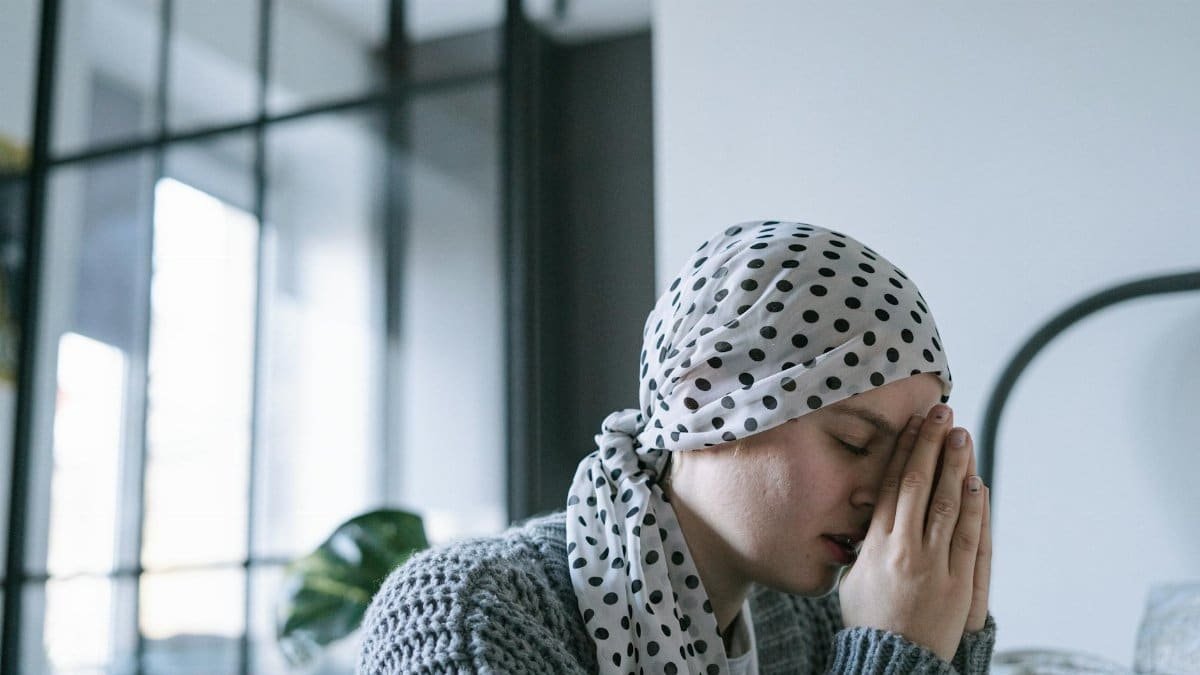 A woman wearing a polka dot scarf prays with hope, symbolizing strength and recovery during illness.