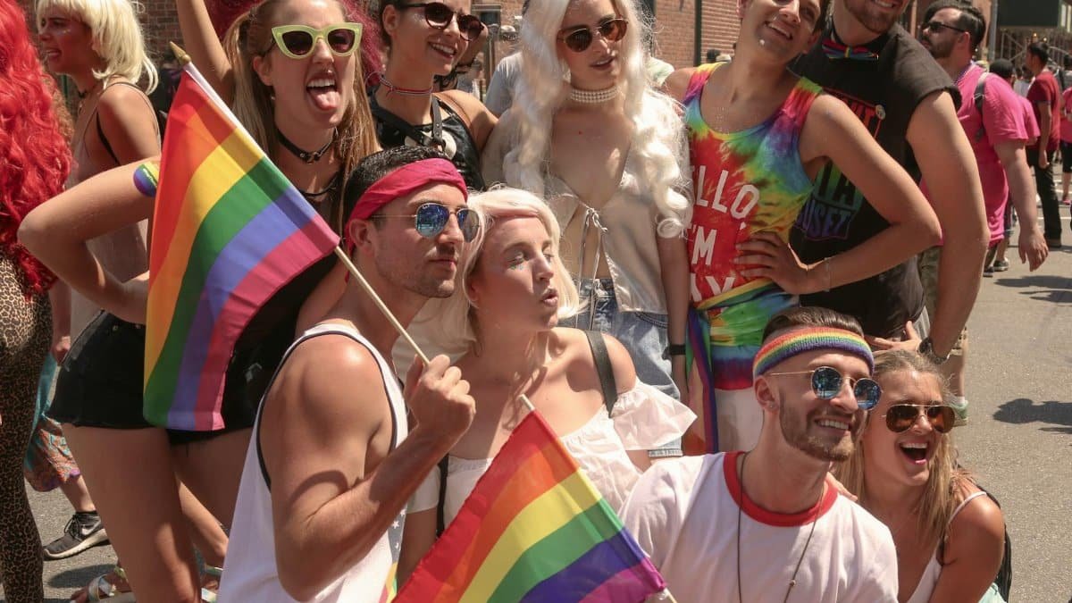 Group of diverse people celebrating at the NYC Pride Parade, waving rainbow flags.