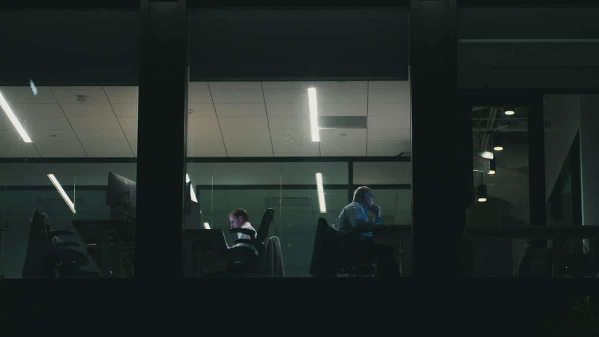 Two people working late in a modern Houston office building, visible through a window.