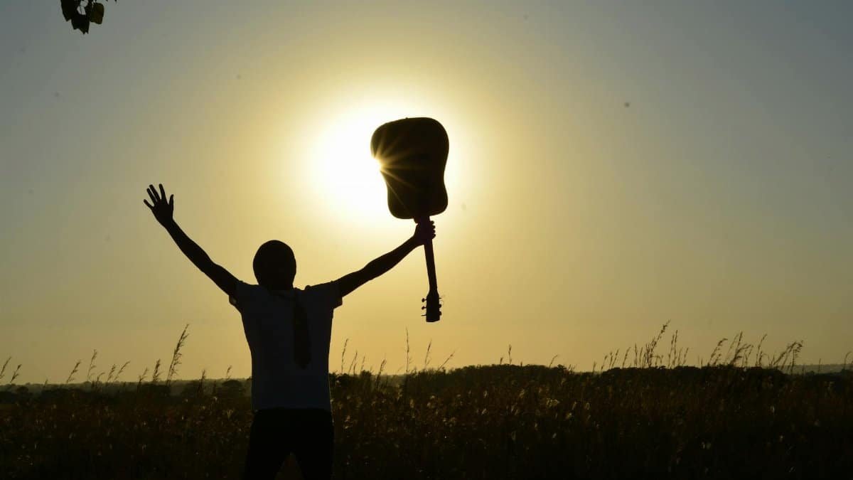 A young guitarist celebrates the sunrise with an acoustic guitar, creating a dramatic silhouette.