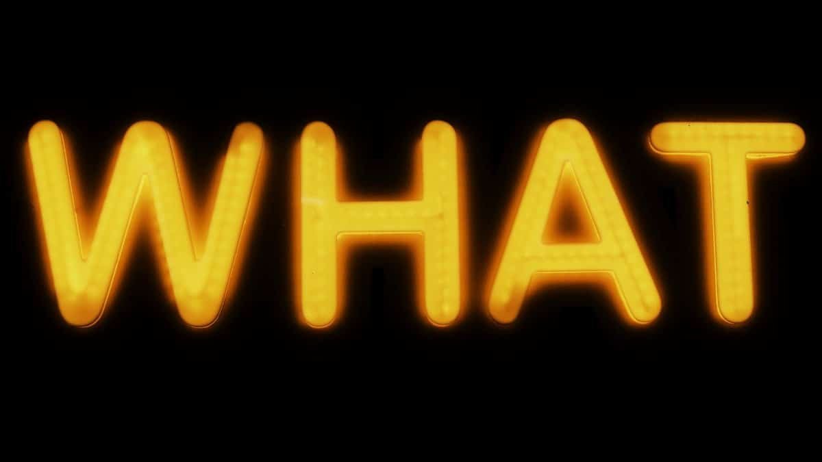 Bright yellow neon 'What' sign glowing against a black background in Budapest, Hungary.