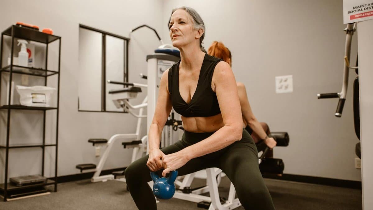 Active senior woman performing kettlebell squats for strength training at indoor gym.