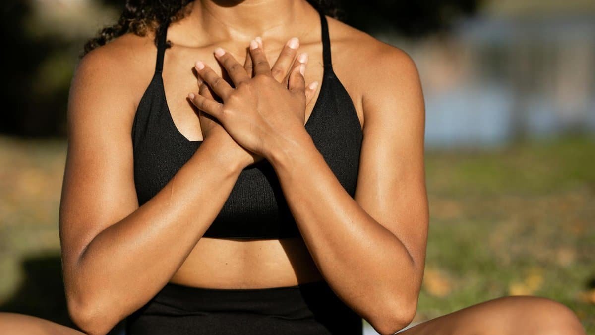 A woman in activewear practices mindfulness meditation outdoors, hands on chest.