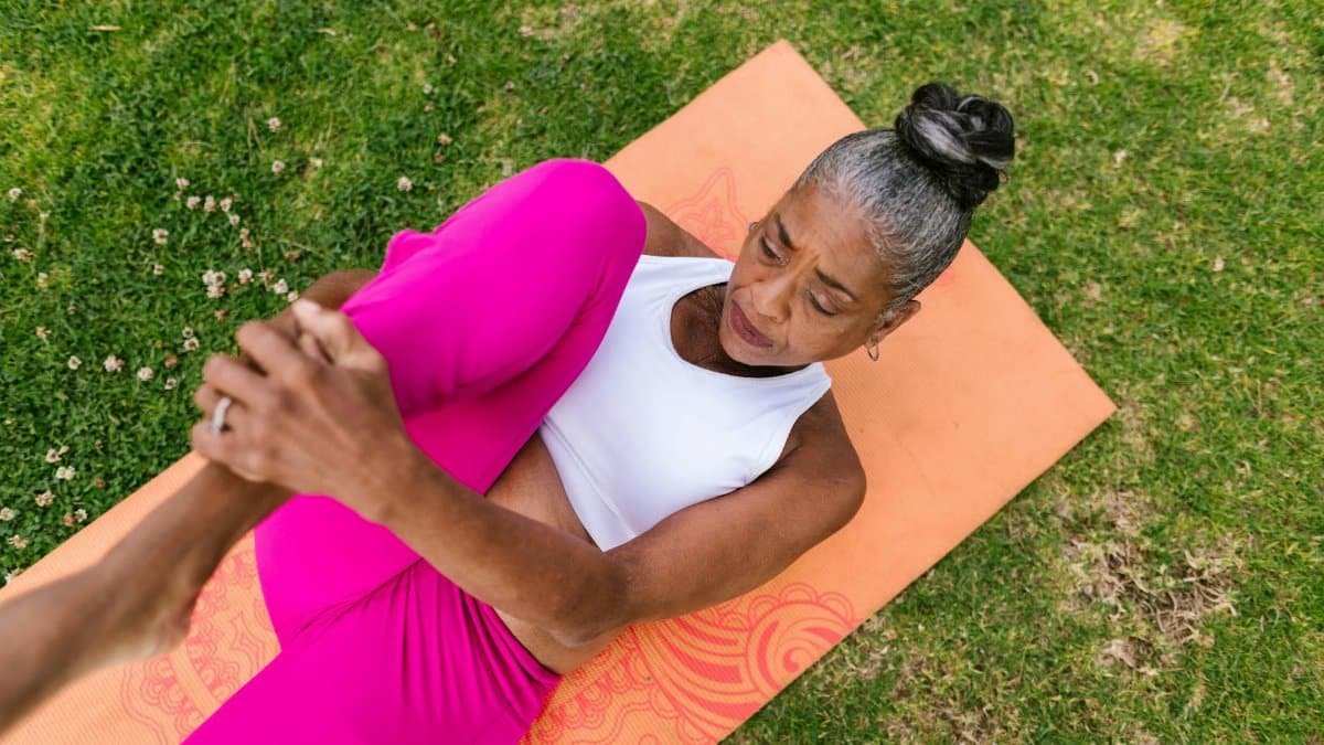 Elderly woman performing yoga stretch on grass for wellness.