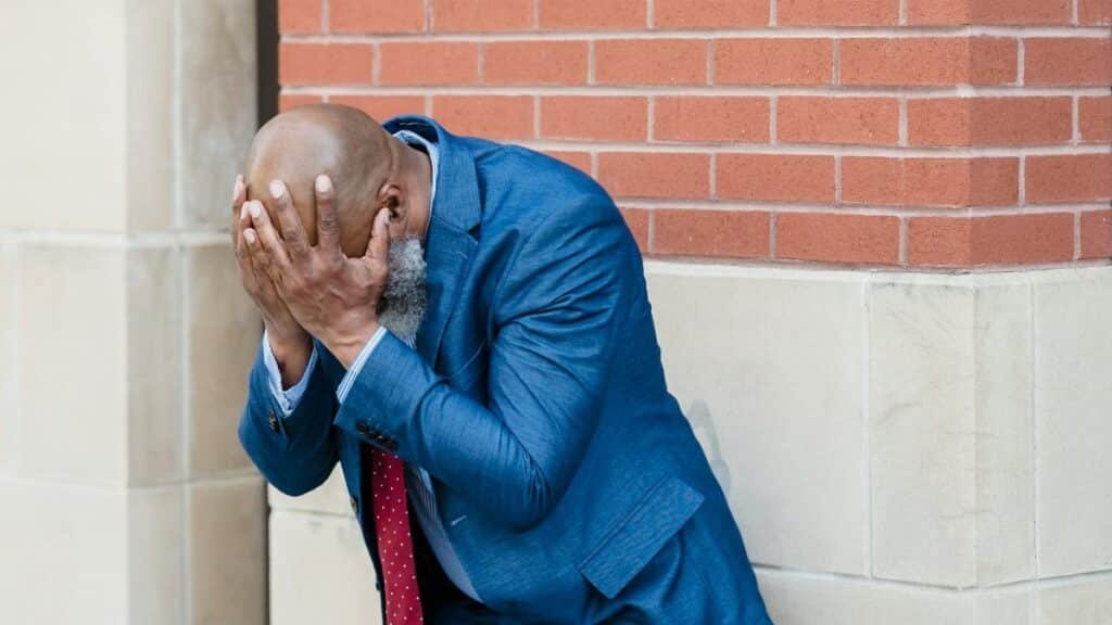 Businessman in blue suit shows stress and concern against urban background.