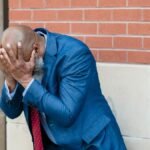 Businessman in blue suit shows stress and concern against urban background.