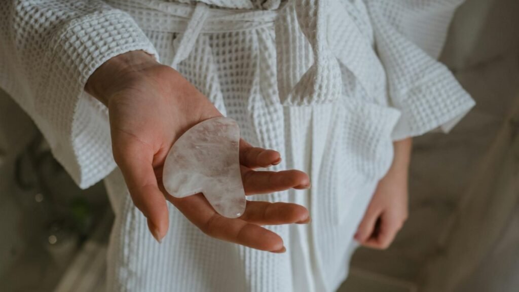 Close-up of a woman's hand holding a gua sha stone, wearing a white bathrobe for skincare routine.