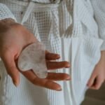 Close-up of a woman's hand holding a gua sha stone, wearing a white bathrobe for skincare routine.