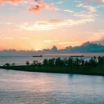 A tranquil ocean sunset over Honolulu with silhouettes of ships and clouds.