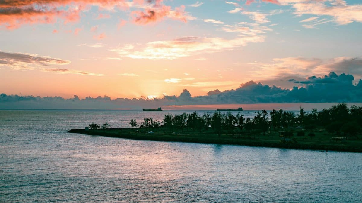 A tranquil ocean sunset over Honolulu with silhouettes of ships and clouds.