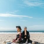Women practicing meditation and crystal healing on a sunny beach.