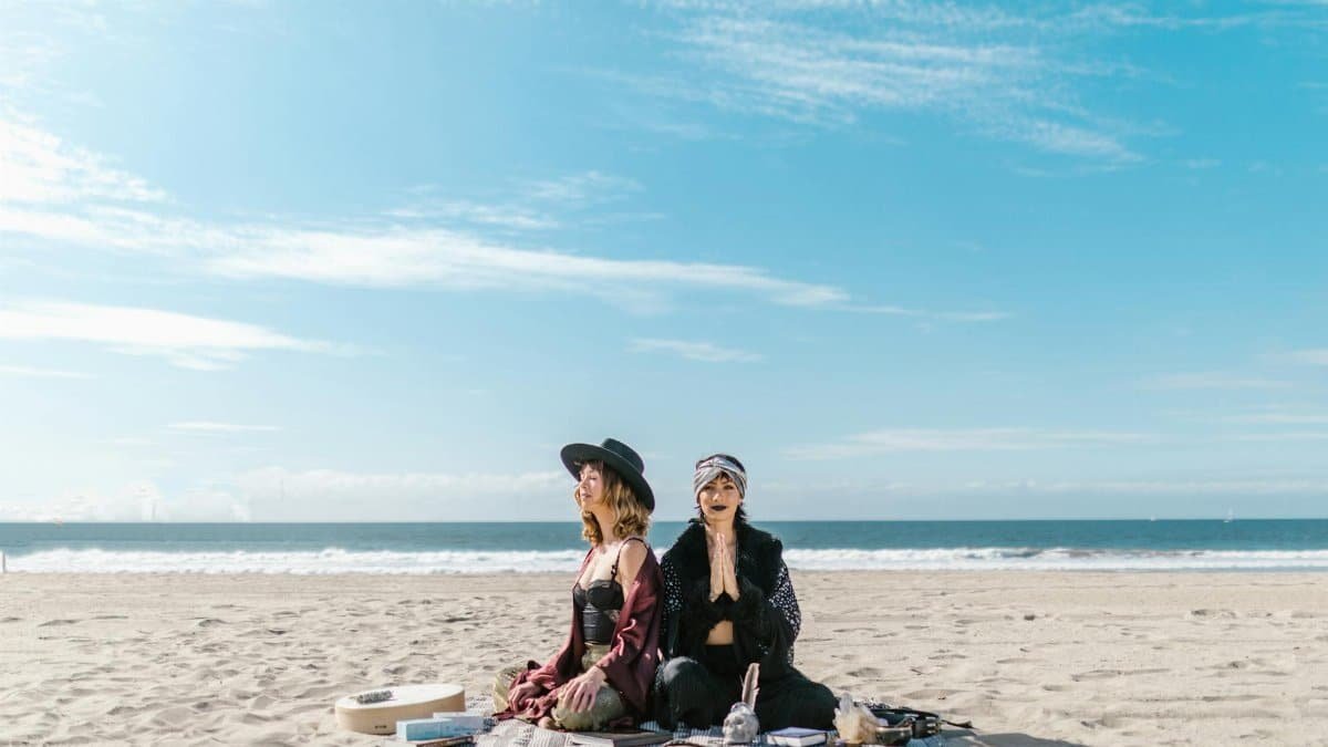 Women practicing meditation and crystal healing on a sunny beach.
