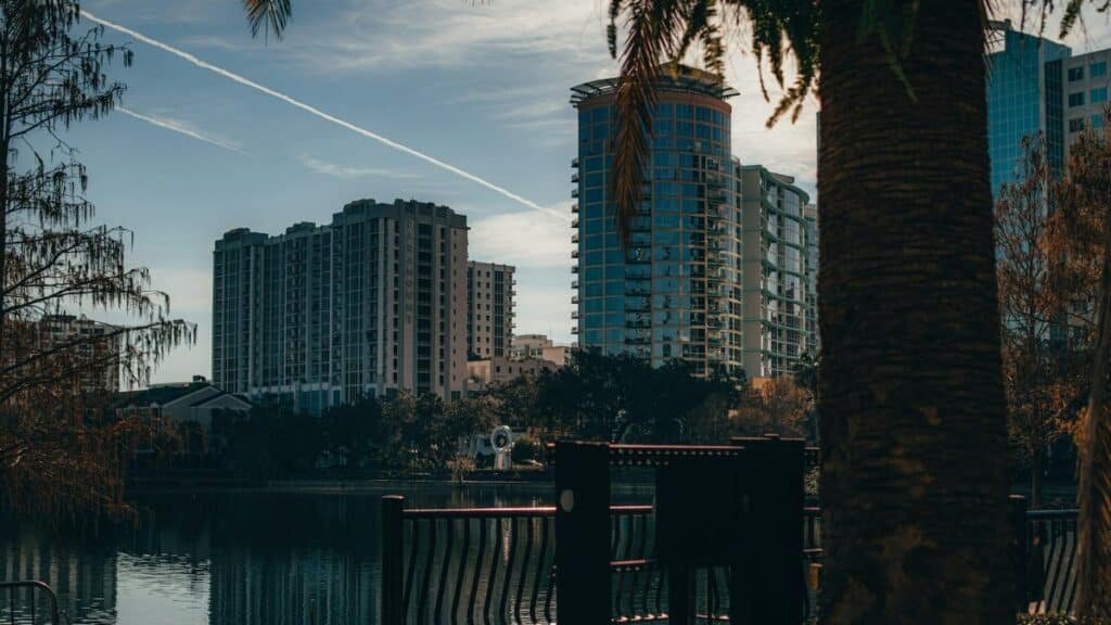View of Orlando's modern skyline reflecting on a tranquil lake, surrounded by trees.