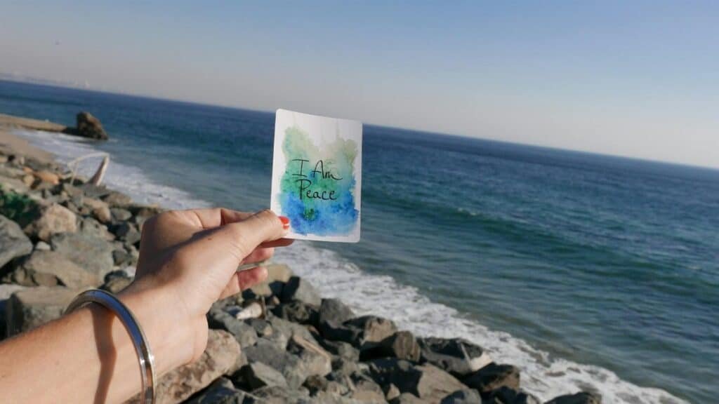 A hand holds a peace card with the ocean view in Malibu, California.