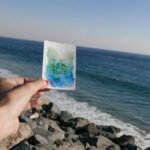 A hand holds a peace card with the ocean view in Malibu, California.