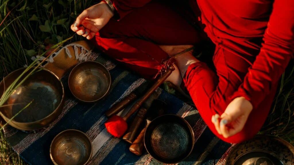 A person meditating outdoors with Tibetan singing bowls, creating a peaceful atmosphere.