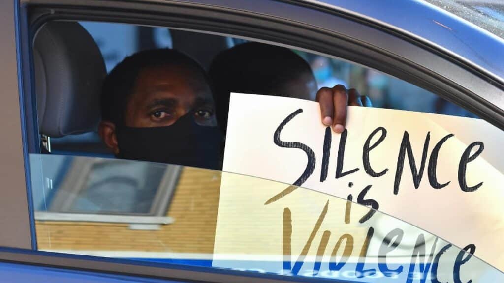 Black man in a car holds a 'Silence is Violence' protest sign in Chicago.
