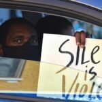 Black man in a car holds a 'Silence is Violence' protest sign in Chicago.
