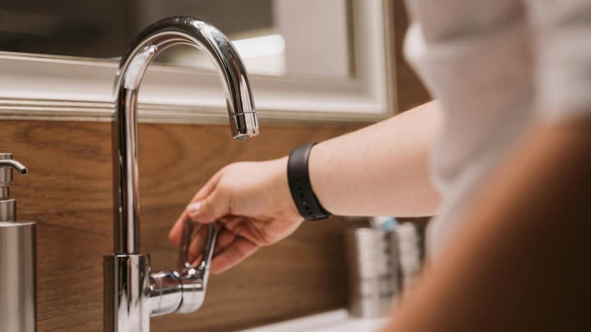 Close-up of a person's hand turning a chrome faucet handle in a modern bathroom setting.