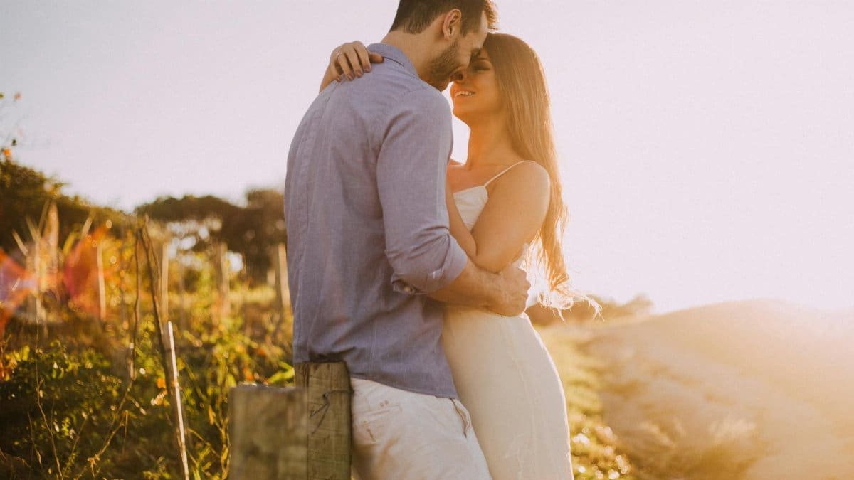 A couple shares a romantic moment embracing at sunset outdoors with warm light.