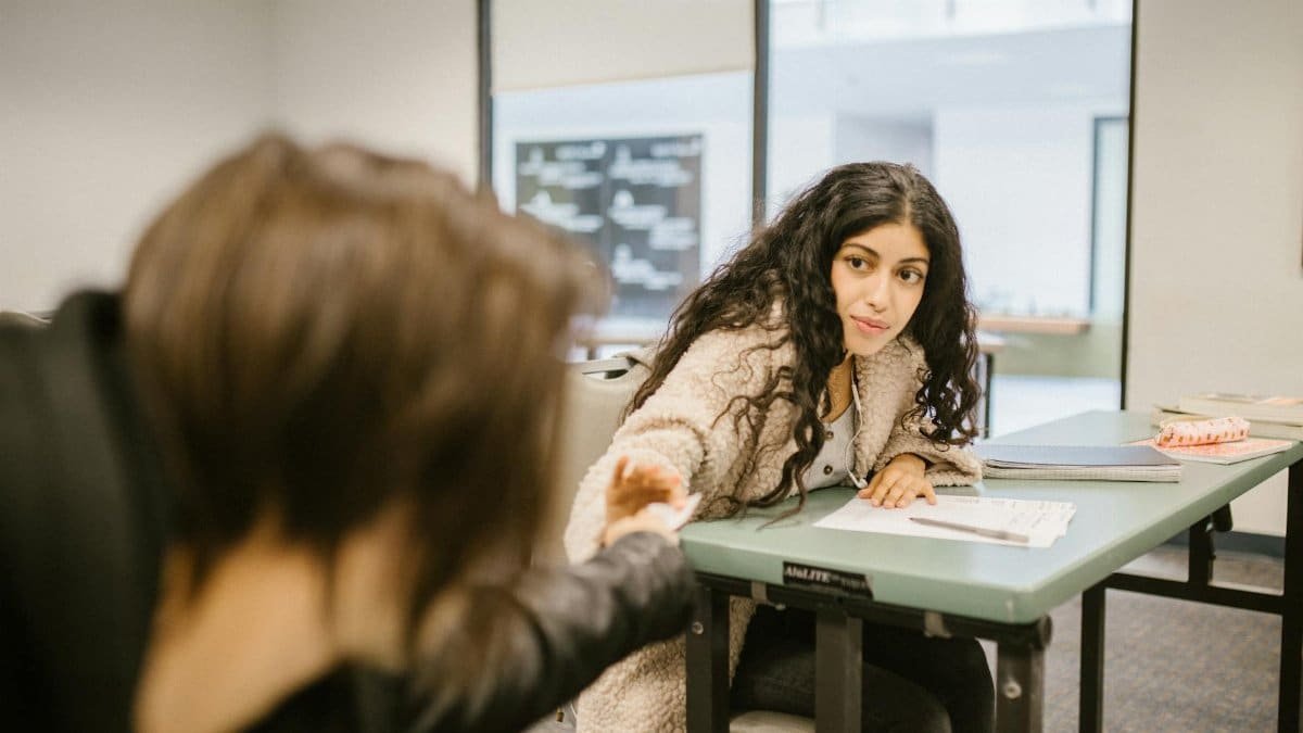 Two college students discreetly pass notes during a classroom exam, symbolizing cheating.