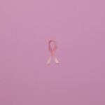 Pink ribbon on pastel background symbolizing breast cancer awareness.