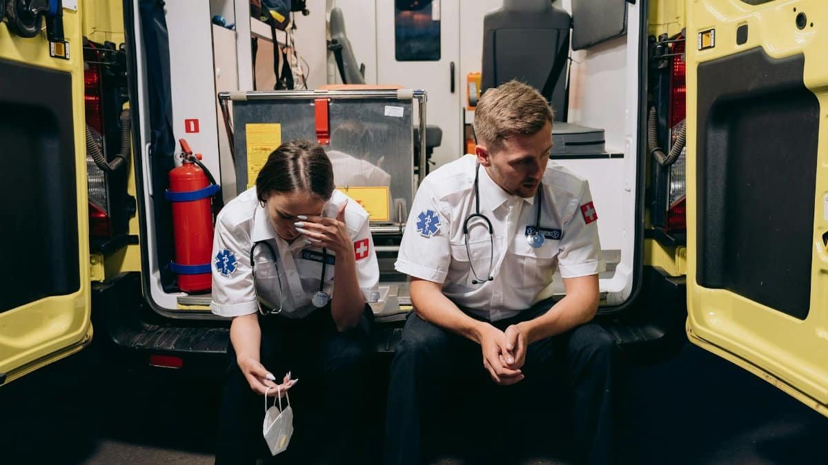 Two paramedics sitting tired at the back of an ambulance, reflecting the stress of emergency services.