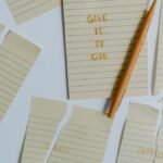 Ripped notebook pages with words anxiety, stress, depression, give it to God and a pen on a table.