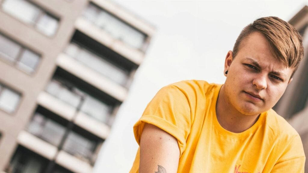 Young adult in yellow shirt posing with modern building in background.