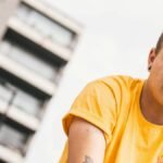 Young adult in yellow shirt posing with modern building in background.