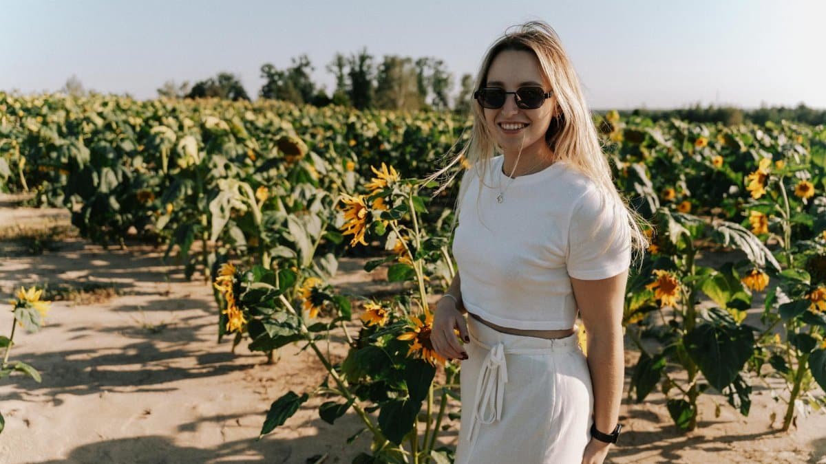 A young woman smiles amid vibrant sunflowers under a clear sky, enjoying a sunny summer day.