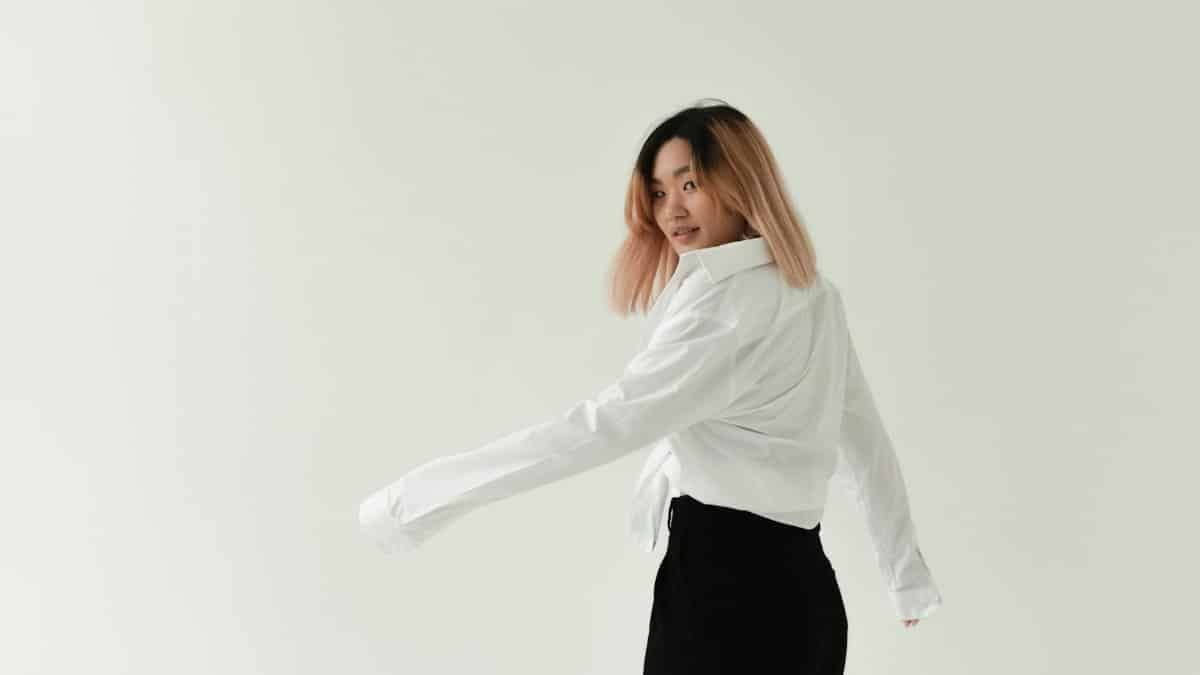 Asian woman in a white shirt turning with a confident pose against a minimalist studio background.