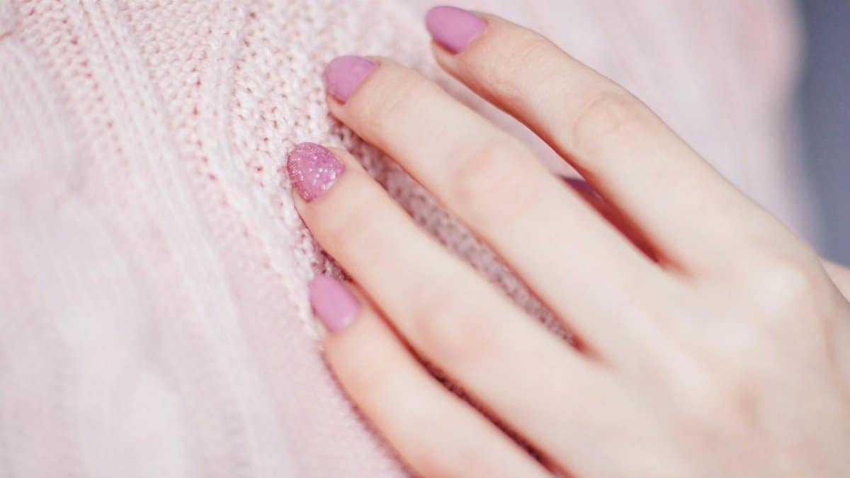 Close-up of a woman's hand with pink manicure resting on a soft knit sweater, showcasing elegance and fashion.