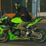 Motorcyclist on a green Kawasaki driving through Houston city streets on a sunny day.