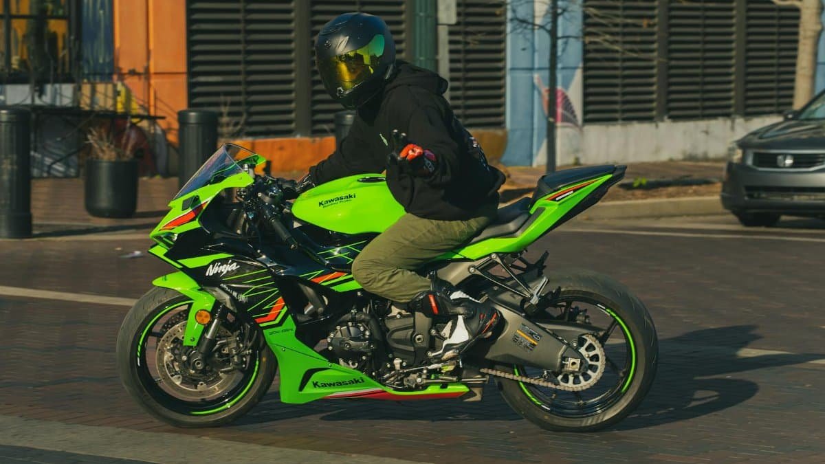 Motorcyclist on a green Kawasaki driving through Houston city streets on a sunny day.