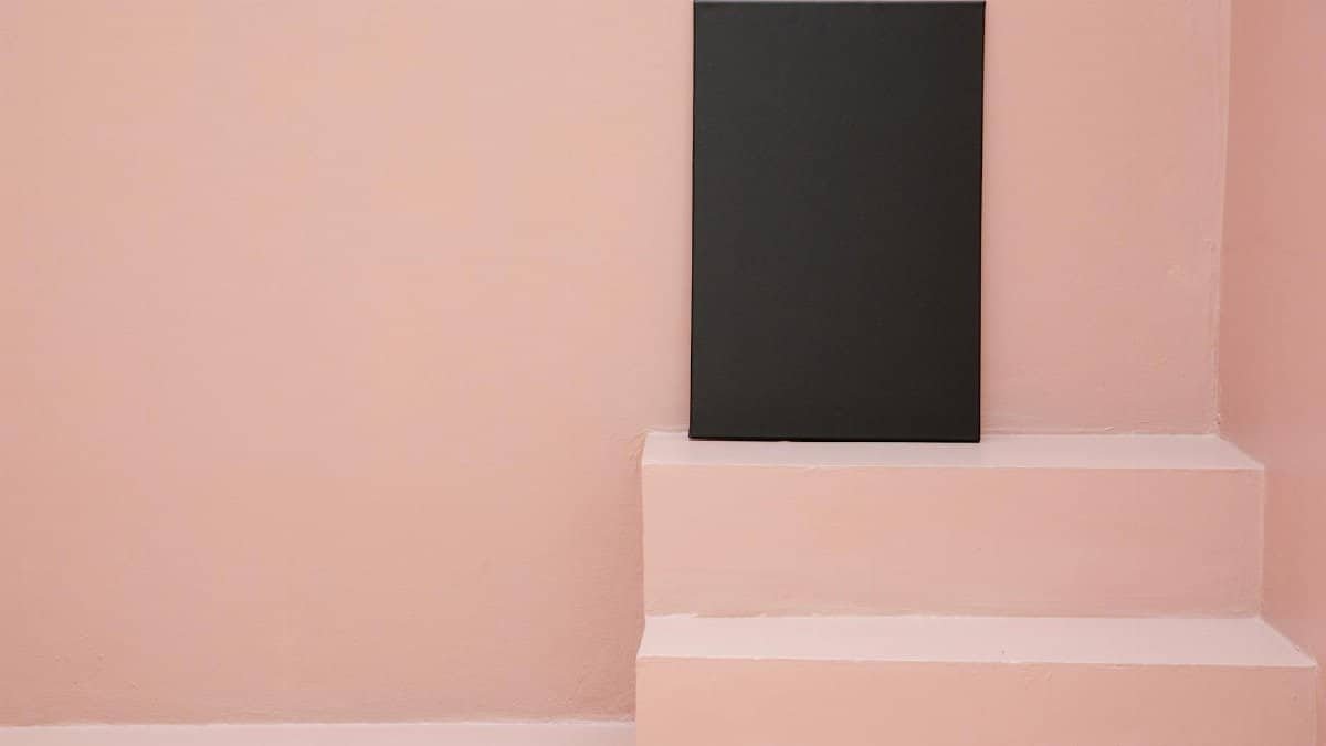 Rectangular blank black canvas placed on stairs against pink background in light room
