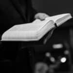 Grayscale close-up of a person holding an open Bible, conveying a sense of faith.