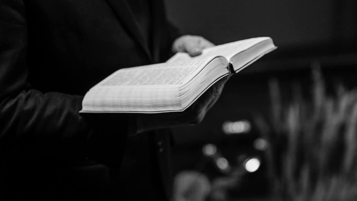 Grayscale close-up of a person holding an open Bible, conveying a sense of faith.