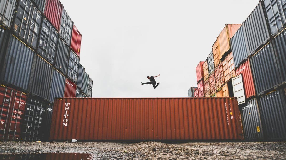 A person leaps dramatically above stacked shipping containers, showcasing freedom and industrial energy.