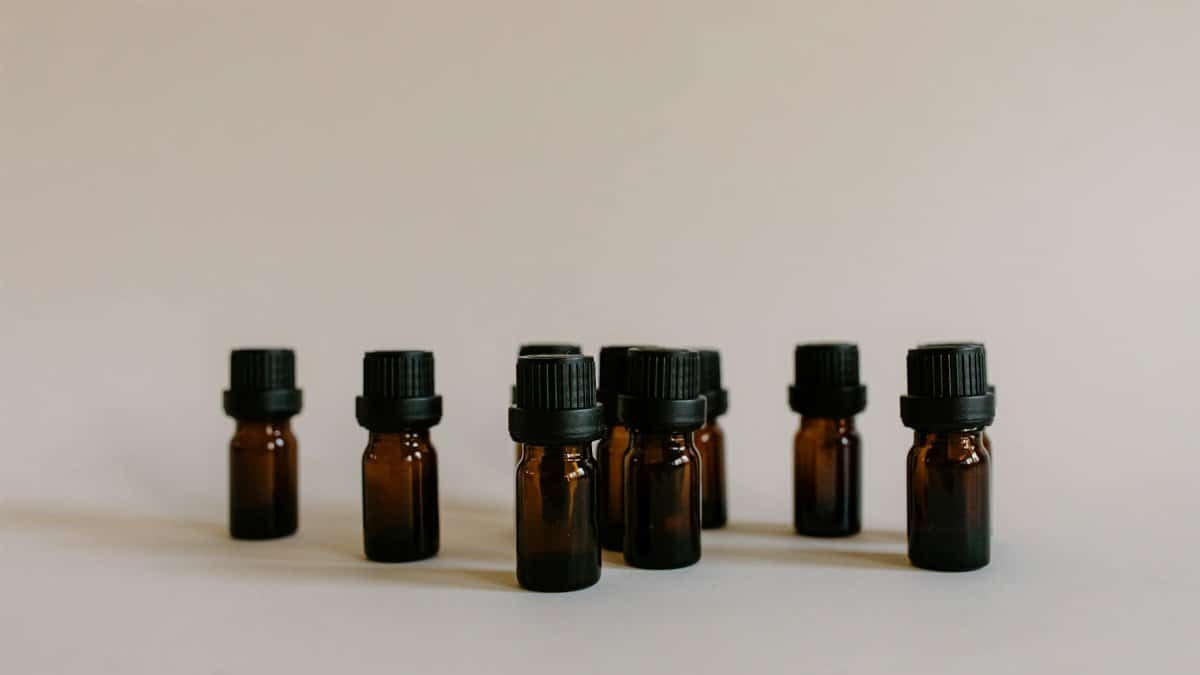 A minimalist still life featuring multiple amber essential oil bottles with black caps on a neutral background.