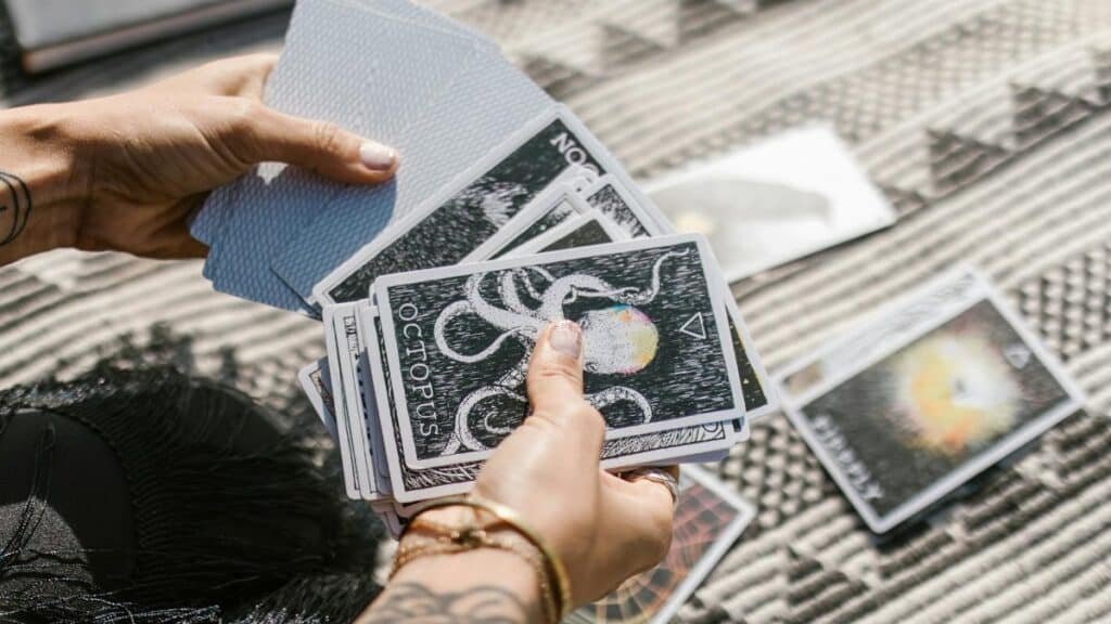 Hands holding tarot cards during a reading session on a patterned mat.