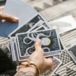 Hands holding tarot cards during a reading session on a patterned mat.