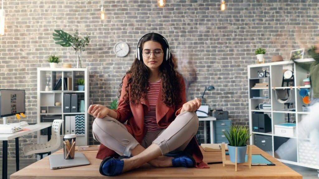 Young woman meditating with headphones in a modern office setting, practicing mindfulness.