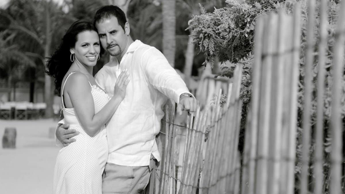 A romantic black and white portrait of a couple embracing near a beach fence in Miami Beach, Florida.
