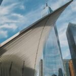 Dramatic angle of New York City's One World Trade Center and surrounding skyscrapers against a blue sky.